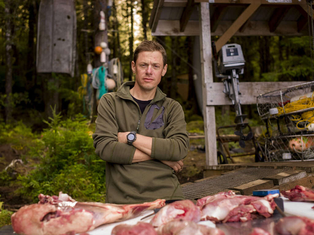 Steven Rinella standing with a butchered deer in the woods.